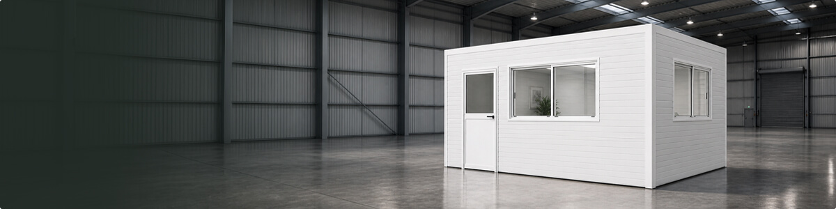 Large industrial warehouse interior with smooth concrete floor and high ceilings, featuring a white prefabricated modular office with windows and door, designed as an enclosed workspace.