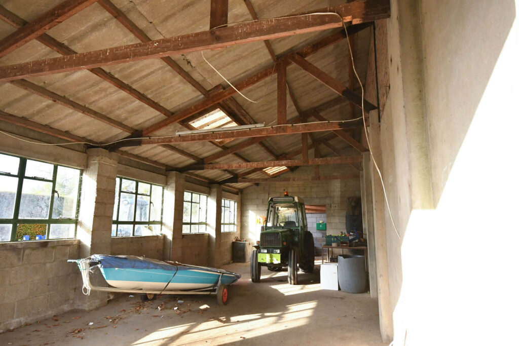 Interior of shed with blue and white boat on dolly and green tractor parked near workbench